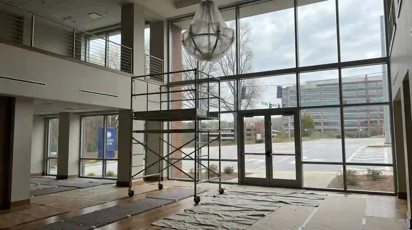 Rolling scaffold in a two-story foyer under a wrapped chandelier